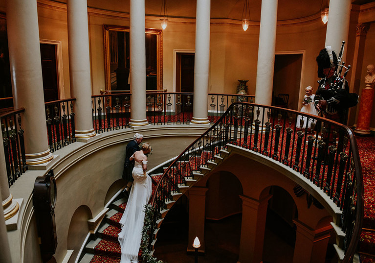 Newlyweds walk up the grand Oval Staircase with moody lighting and columns